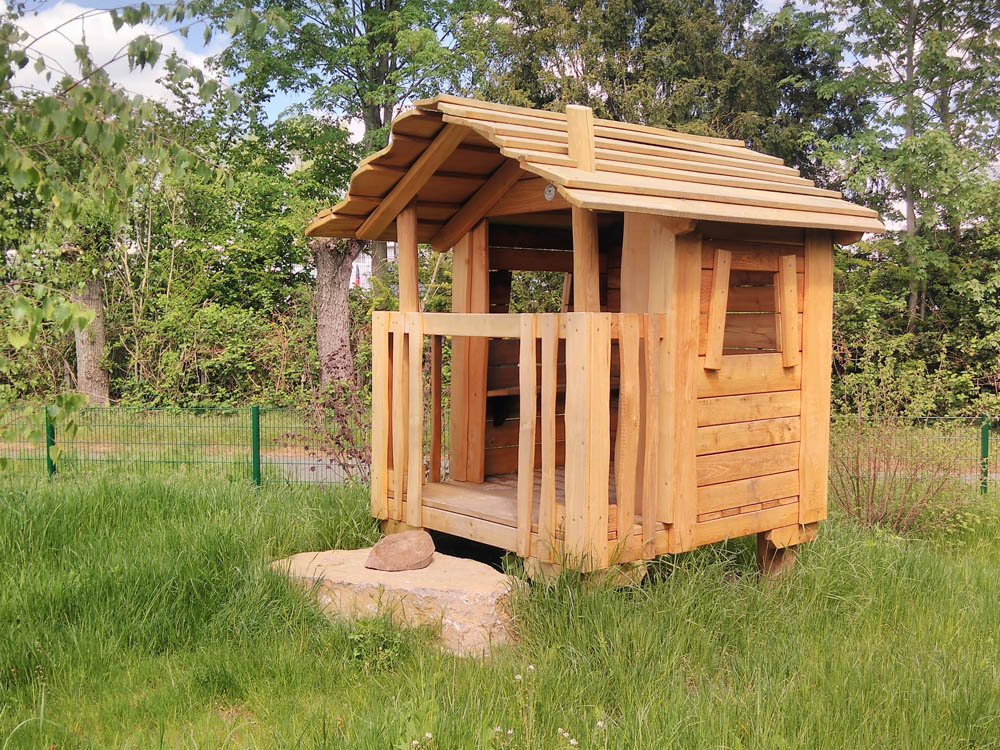 Handgefertigtes Spielhaus aus Holz auf naturnahem Au&szlig;engel&auml;nde mit Grasfl&auml;che